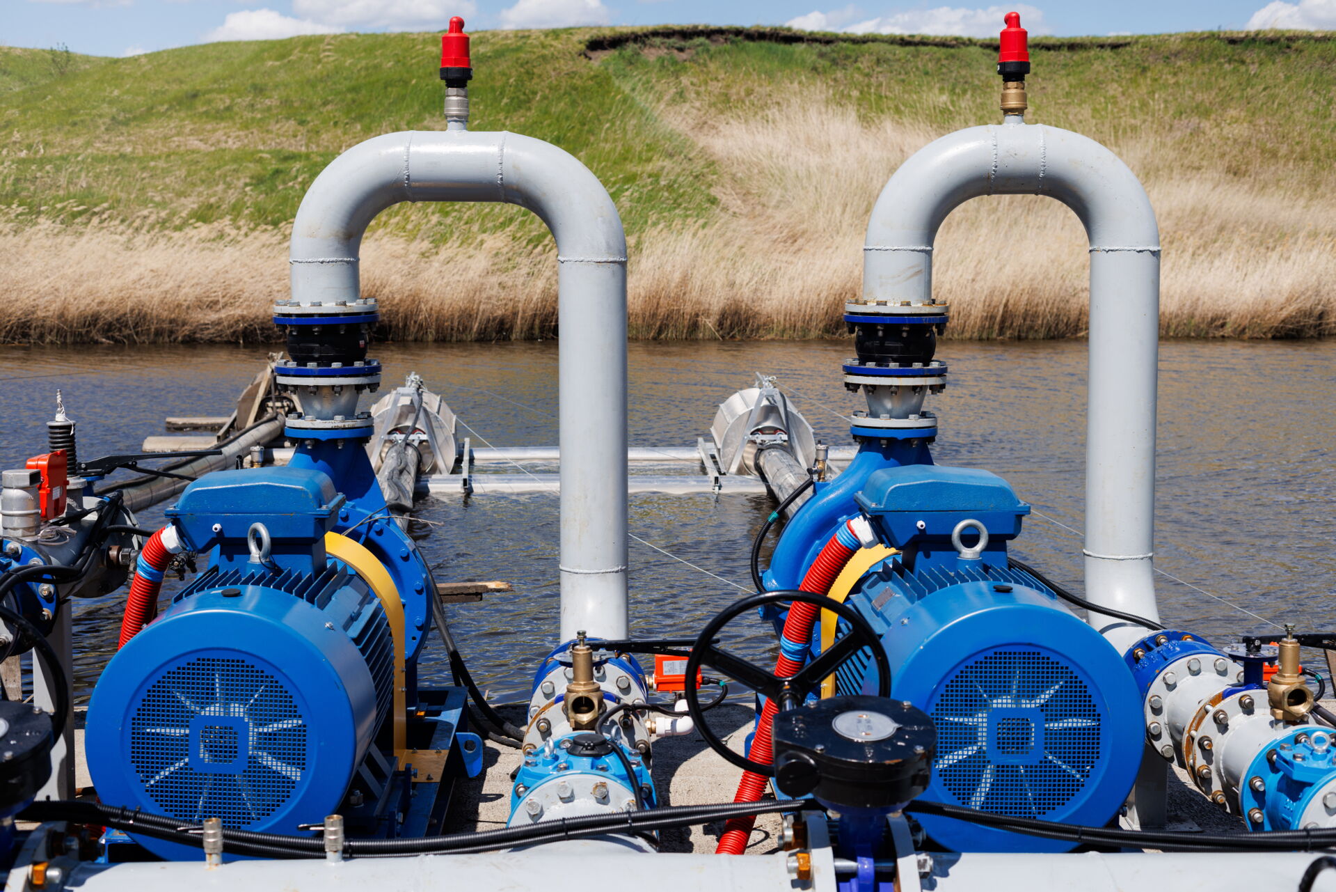 Zwei blaue Elektromotoren als elektrische Antriebe für Wasserpumpen direkt am Ufer - im Hintergrund eine Deichmauer mit Schilfgras